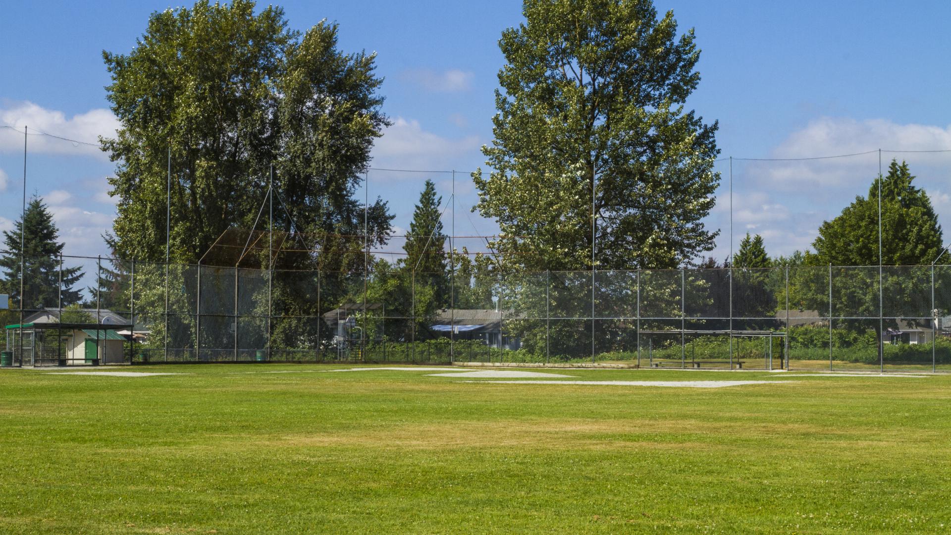A grassy field with a baseball diamond in the corner. 